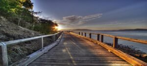 Wooden coastal boardwalk at sunrise overlooking calm water and hills in Australia’s Whitsunday Islands.