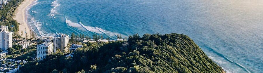 Aerial view of Burleigh Heads with forested headland, long sandy beach, and ocean waves.