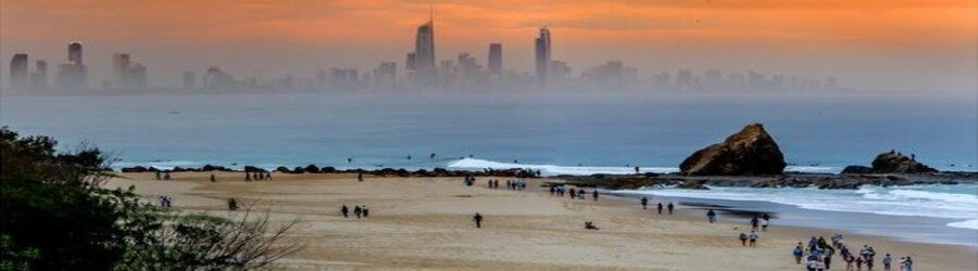 Sunset over Currumbin Beach with glowing sky and distant city skyline.