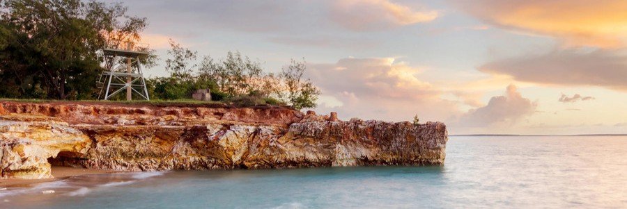 Rocky coastline at East Point Reserve in Darwin, Australia, with calm turquoise water and a colorful sunset.