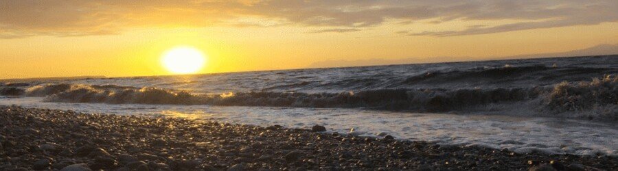 Golden sunset over the waves at Point Woronzof near Anchorage with rocky shoreline in the foreground.