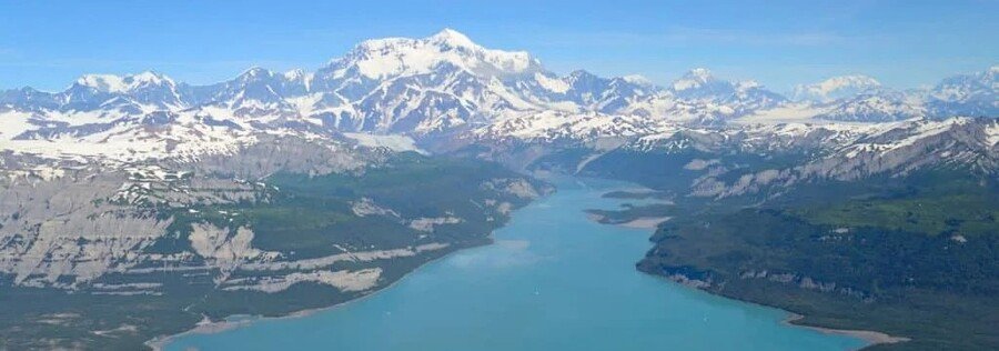 Aerial view of Icy Bay near Yakutat, Alaska, with turquoise glacial water surrounded by snow-capped mountains and rugged coastal wilderness.