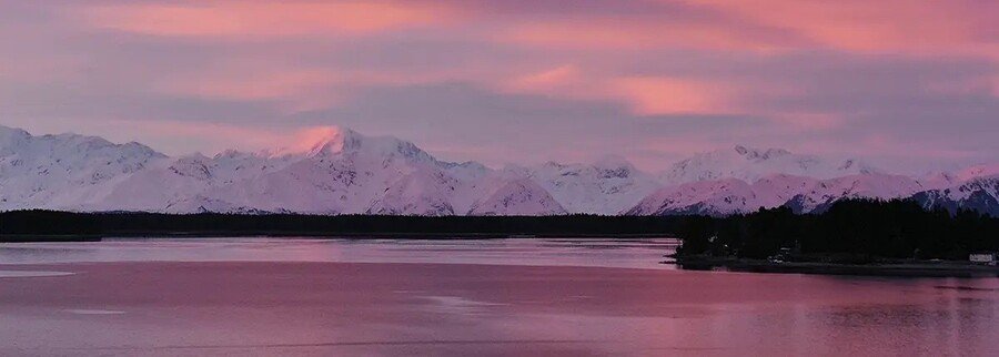Pink sunset over Yakutat Bay with snow-covered Alaska mountains reflecting on calm coastal water