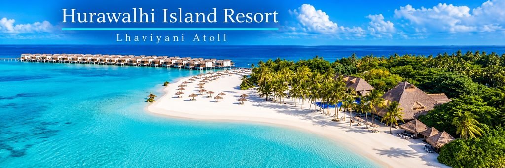 Aerial view of a curved white-sand beach lined with tropical palm trees, thatched-roof resort buildings, and overwater villas beside a turquoise lagoon.