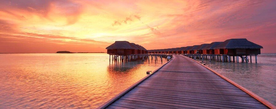 Overwater bungalows at sunset with wooden boardwalk and calm tropical lagoon reflecting colorful sky
