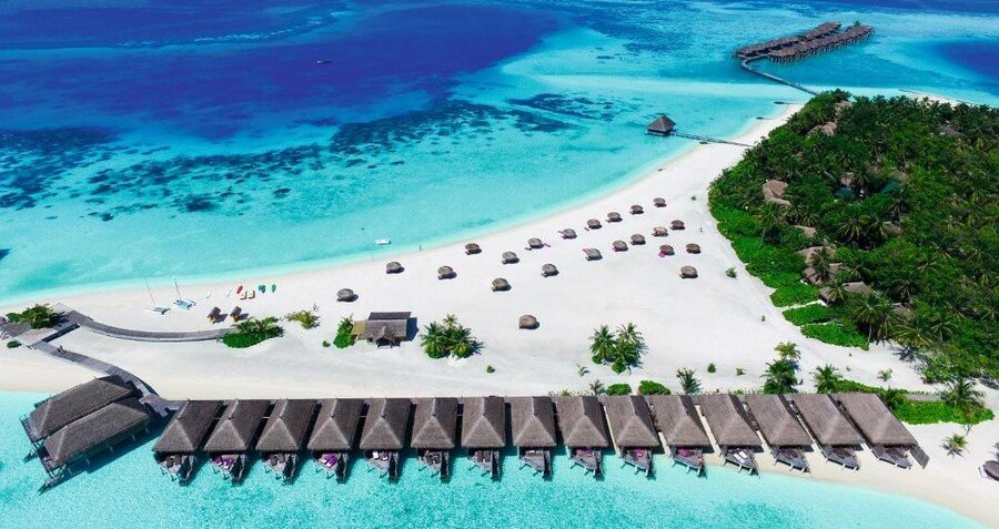 Aerial view of overwater bungalows, white sand beach, turquoise lagoon, and palm-covered tropical island