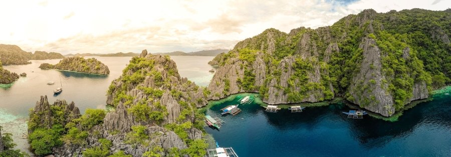 Aerial view of limestone cliffs, lush green islands, and outrigger boats floating in the turquoise waters of Coron, Palawan.