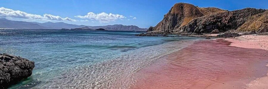 Pink Beach on Komodo Island with soft pink sand, clear turquoise water, and rugged volcanic hills in Indonesia.