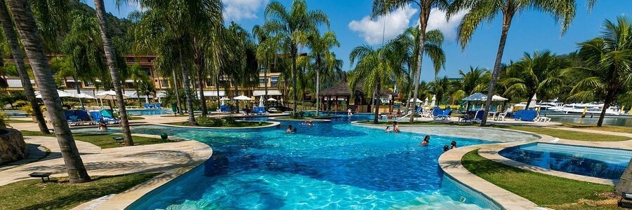 Large freeform resort swimming pool surrounded by palm trees and lounge chairs with guests swimming at Promenade Angra dos Reis in Brazil