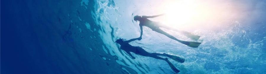 Two snorkelers holding hands underwater in the sunlight.