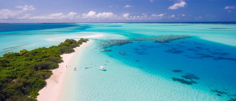 Aerial view of tropical sandbar with shallow turquoise lagoon, small boats, and lush island vegetation