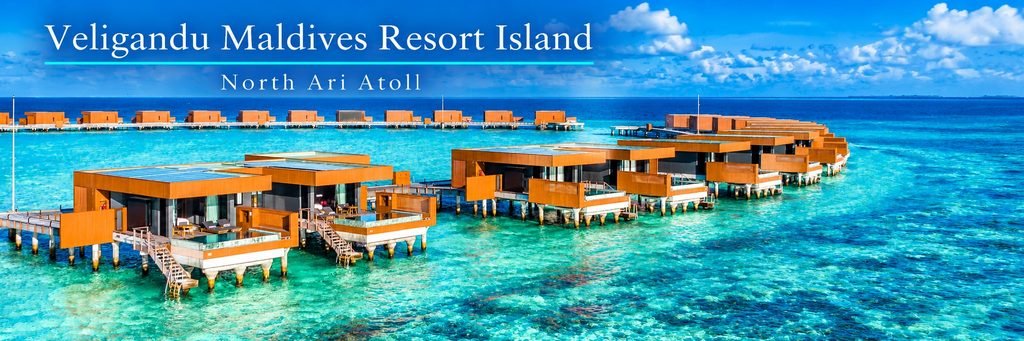 Aerial view of modern wooden overwater villas with private pools, connected by walkways above a brilliant turquoise lagoon with visible coral formations.