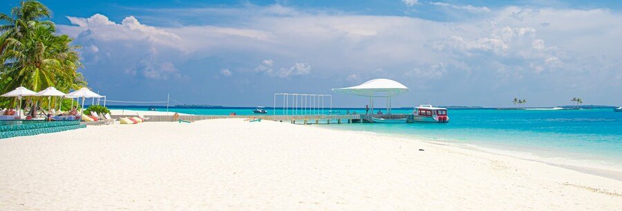 White sand tropical beach with palm trees, turquoise water, lounge chairs, and a pier with boat nearby