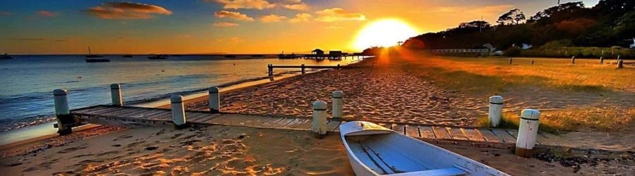 Sunrise over a peaceful beach with a wooden dock and rowboat, showcasing warm golden light and calm coastal scenery.