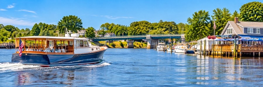 Scenic guided boat tour in Westport, Connecticut, featuring a passenger boat cruising past waterfront homes, marinas, and a bridge along the water.