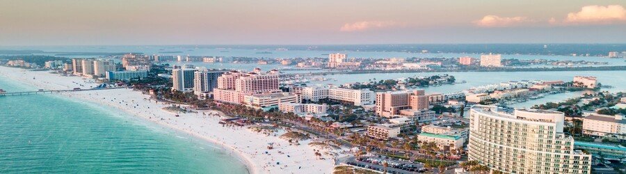 Aerial view of Clearwater Beach with turquoise Gulf water, beachfront resorts, and a pastel sunset sky.