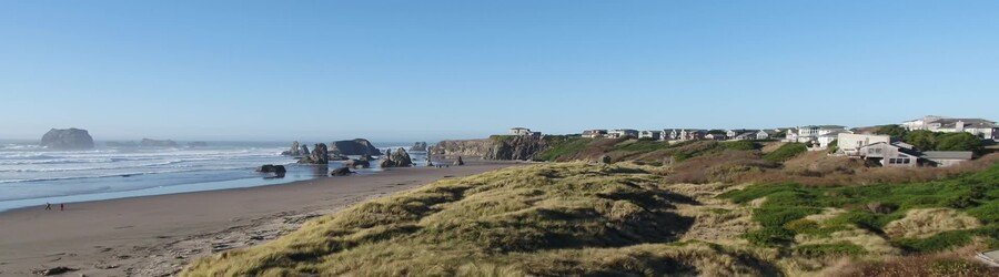 Oregon coast beach town with dramatic sea stacks, rolling dunes, and homes overlooking the shoreline.
