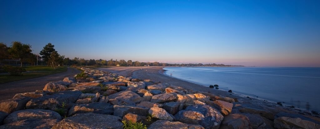 Sherwood Island State Park beach in Westport Connecticut with rocky shoreline, calm water, and sunset coastal scenery