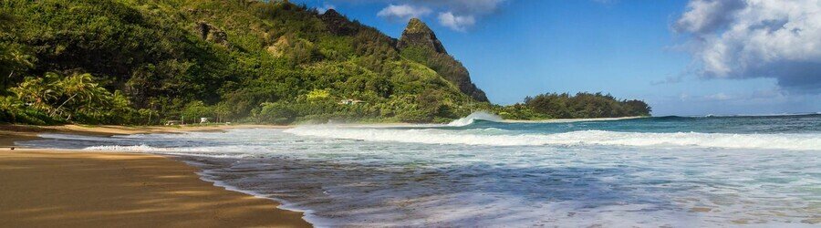 Makua Tunnels Beach in Kauai with turquoise waves, lush mountains, and wide sandy shoreline.