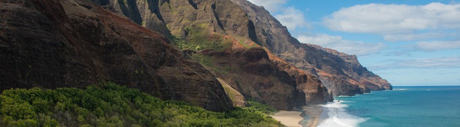 Nāpali Coast cliffs rising above a remote beach and deep blue ocean on Kauai.