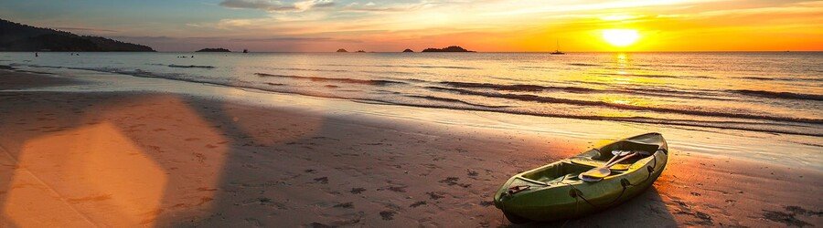 Kayak resting on the sand at sunset on a quiet Maui beach with golden light over the ocean.