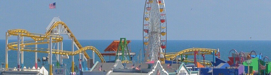 Colorful roller coaster and Ferris wheel at the Santa Monica Pier by the ocean.