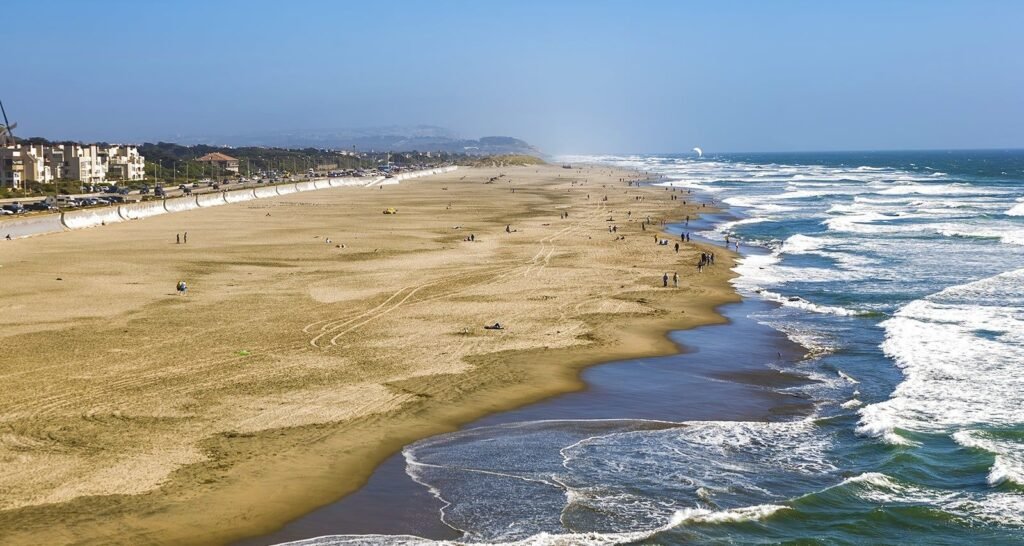 Wide sandy shoreline at Ocean Beach in San Francisco with waves and distant visitors.