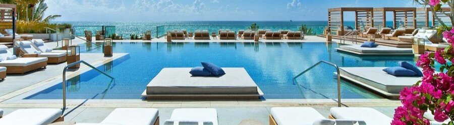 Modern oceanfront pool deck with white sun loungers and pink bougainvillea at Andaz Miami Beach Resort