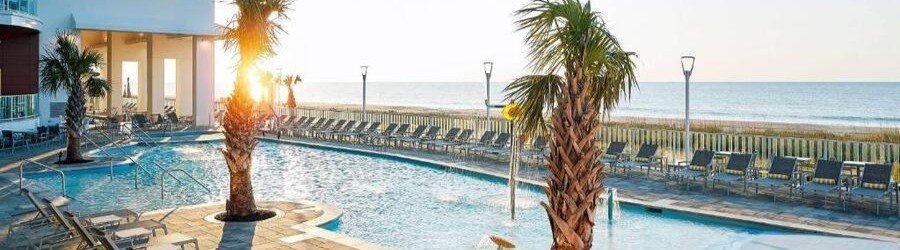 Sunlit oceanfront pool deck with palm trees and sun loungers facing the beach at Hilton Grand Vacations Club Ocean 22