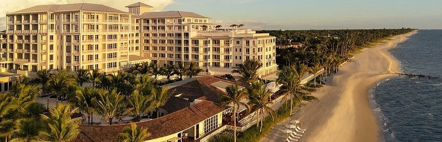 Golden hour view of the luxury oceanfront hotel facade and white sand beach at Naples Beach Club A Four Seasons Resort