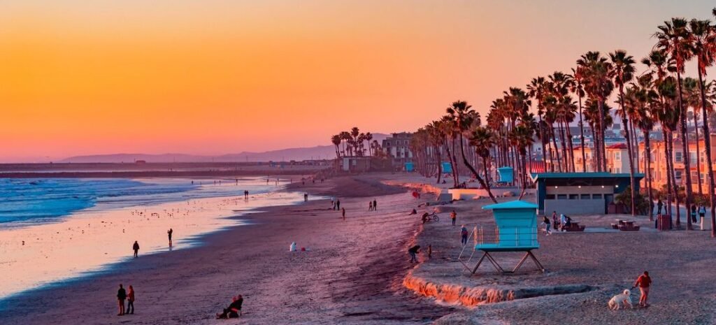 Oceanside California beach at sunset with palm trees, lifeguard towers, and people walking beside the ocean