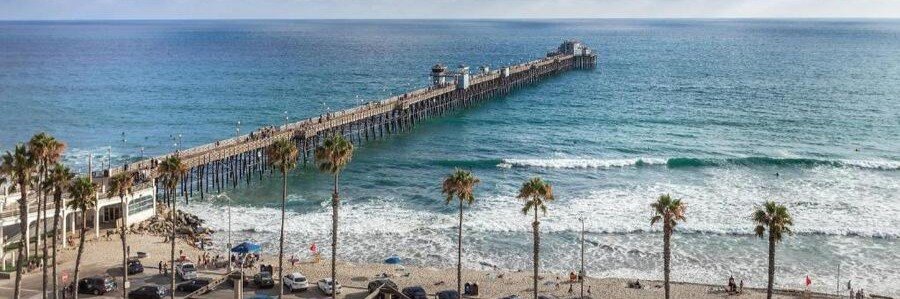 Oceanside California Pier stretching over the Pacific Ocean with waves, sandy beach, and palm trees