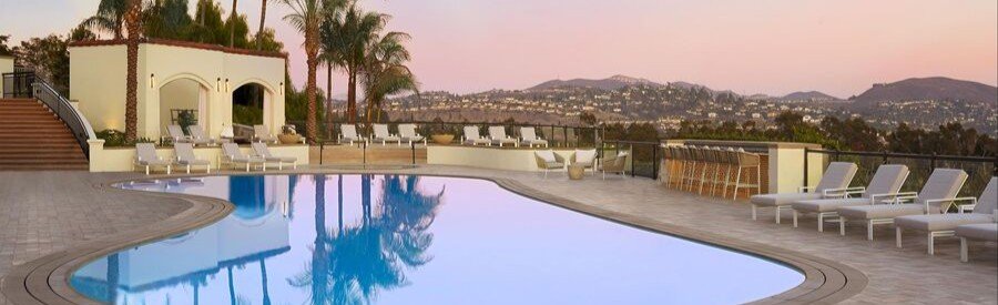 Outdoor pool at Park Hyatt Aviara Resort in Carlsbad with white lounge chairs, palm trees, hills, and a pastel evening sky.