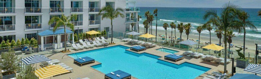 Oceanfront pool at The Seabird Ocean Resort & Spa in Oceanside with cabanas, striped umbrellas, palm trees, and beach views.