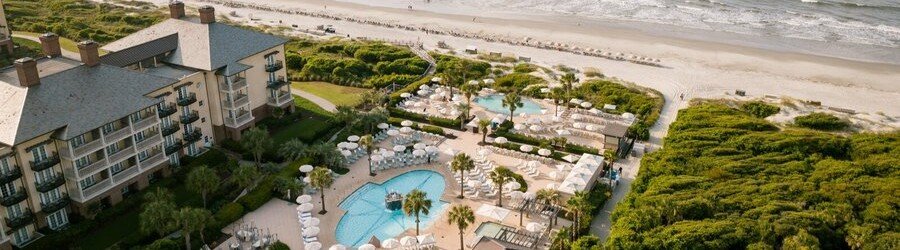 Aerial view of oceanfront pools and grand brick hotel wings at The Sanctuary at Kiawah Island Golf Resort