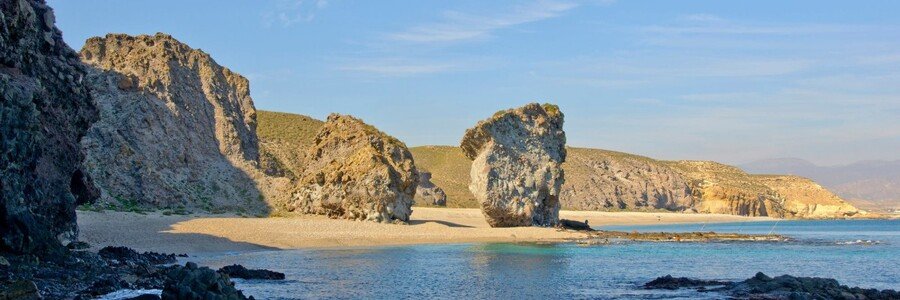Volcanic rock formations and golden sand at Playa de Mónsul in Cabo de Gata Natural Park, Almería, Spain.