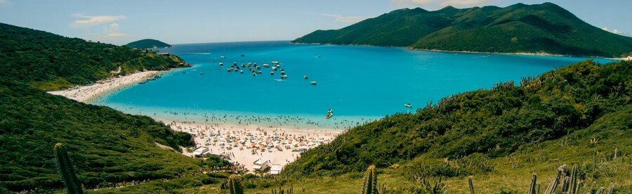 High angle panorama of Prainhas do Pontal do Atalaia in Arraial do Cabo Brazil showing turquoise bay and white sand beach framed by green hills