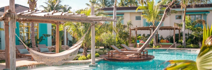 A woven hammock under a rustic wooden pergola next to a tropical outdoor swimming pool at Boardwalk Boutique Hotel Aruba.