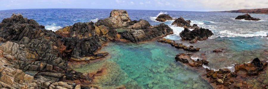 Clear turquoise waters of the Conchi Natural Pool surrounded by volcanic rock formations on the rugged coastline of Aruba.
