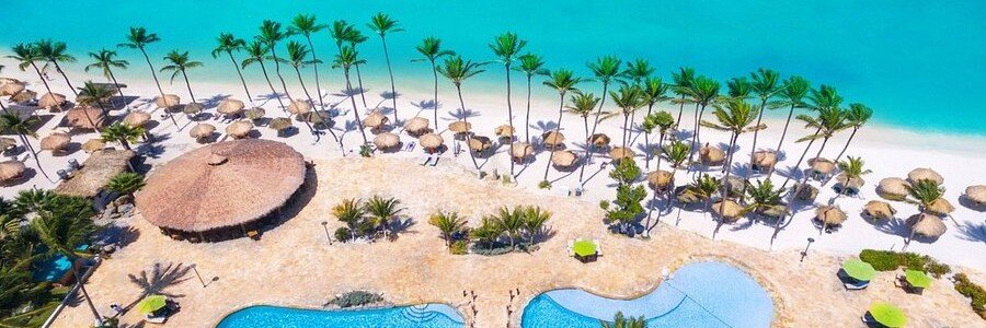 Aerial view of the curvilinear outdoor swimming pools, large thatched beachfront palapas, and pristine ocean waters at Holiday Inn Resort Aruba.