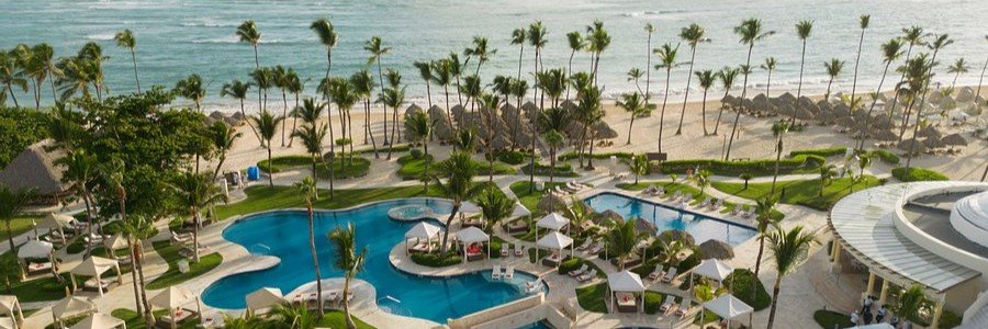 Aerial view of the expansive outdoor swimming pools, cabanas, palm trees, and beachfront at JOIA Bávaro by Iberostar in Punta Cana.