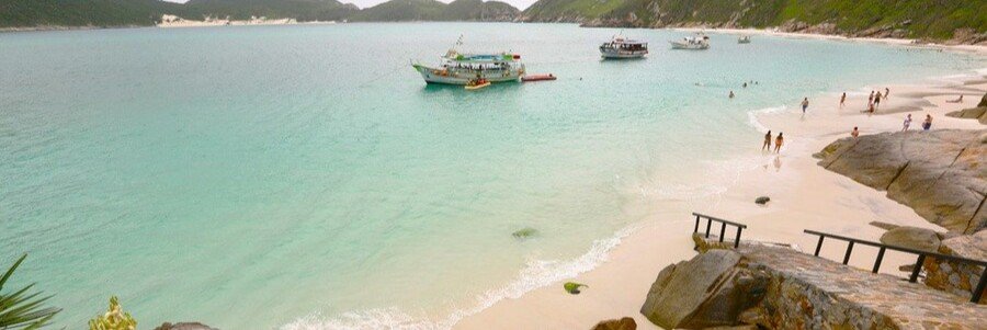 Tour boats anchored in the crystal-clear turquoise waters of Praia do Forno beach in Arraial do Cabo.