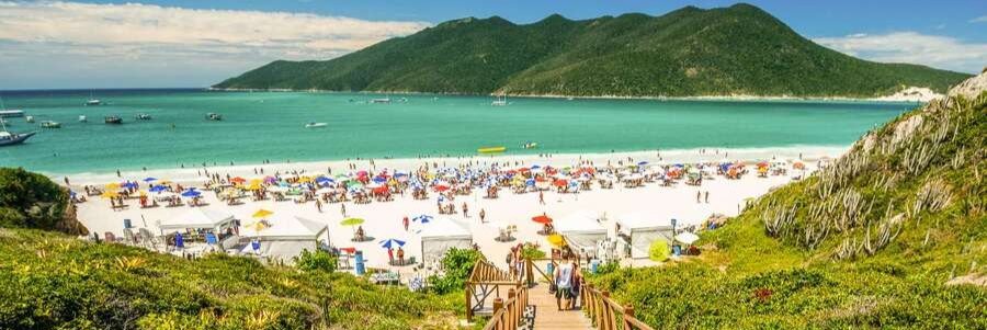 Crowded white sand beach and turquoise water at Prainhas do Pontal do Atalaia viewed from the top of the wooden stairs in Arraial do Cabo.