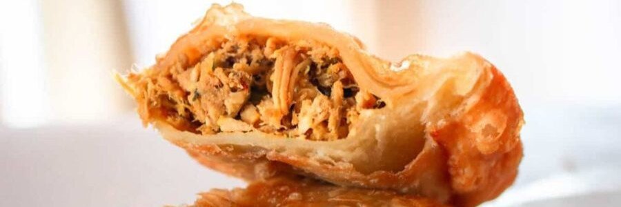 A golden brown, deep-fried Aruban pastechi pastry cut in half to show a savory shredding chicken filling.