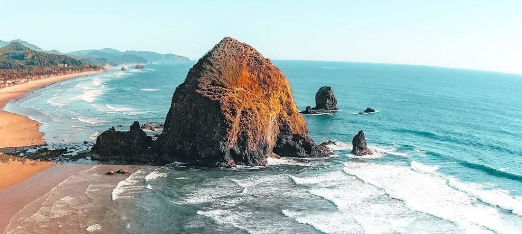 Waves rolling onto the sandy shore at Cannon Beach, Oregon, with Haystack Rock rising from the sea. One of the best American Beaches.
