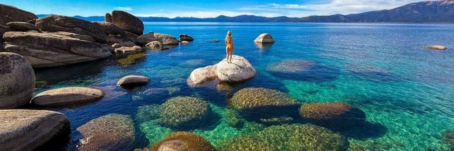 Woman standing on granite boulders overlooking the crystal-clear waters of Sand Harbor at Lake Tahoe, Nevada.