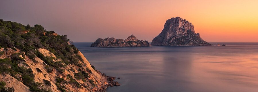 Rocky mystical island of Es Vedra rising from the calm sea at sunset in Ibiza