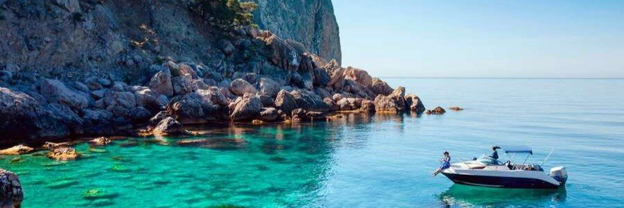 Small motorboat floating on clear turquoise water next to rocky cliffs with Ibiza Water Tours