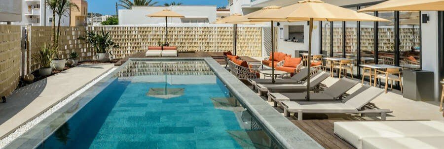 Modern outdoor swimming pool with lounge beds and tan umbrellas at Mirador de Dalt Vila – Relais & Châteaux
