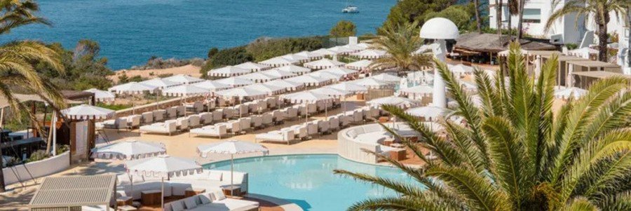 Sprawling outdoor pool club area with white daybeds, matching umbrellas, and palm trees at Montesol Experimental Ibiza